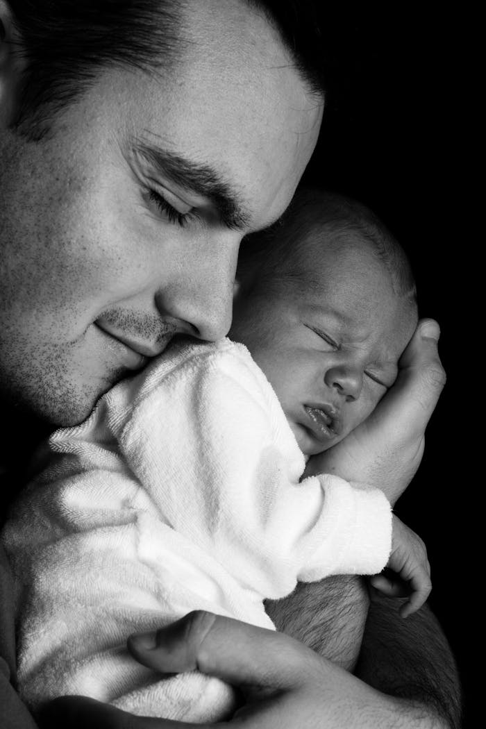 A father lovingly embraces his newborn. Monochrome portrait capturing family warmth.