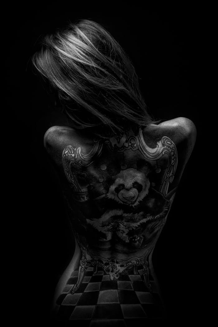 Artistic black and white photo of a woman's tattooed back against a dark background.