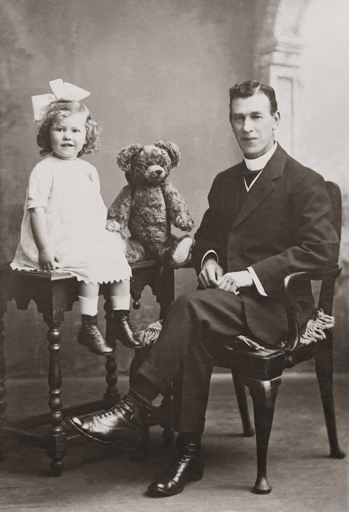 Classic black and white photo of a father and daughter with a teddy bear in a studio setting.