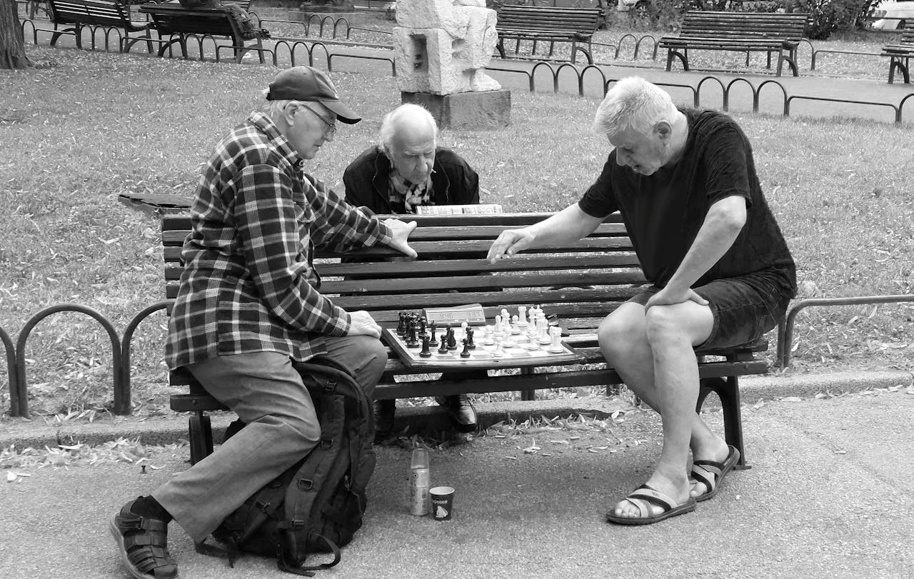 Three elderly men engaged in a serious chess game in a public park setting.